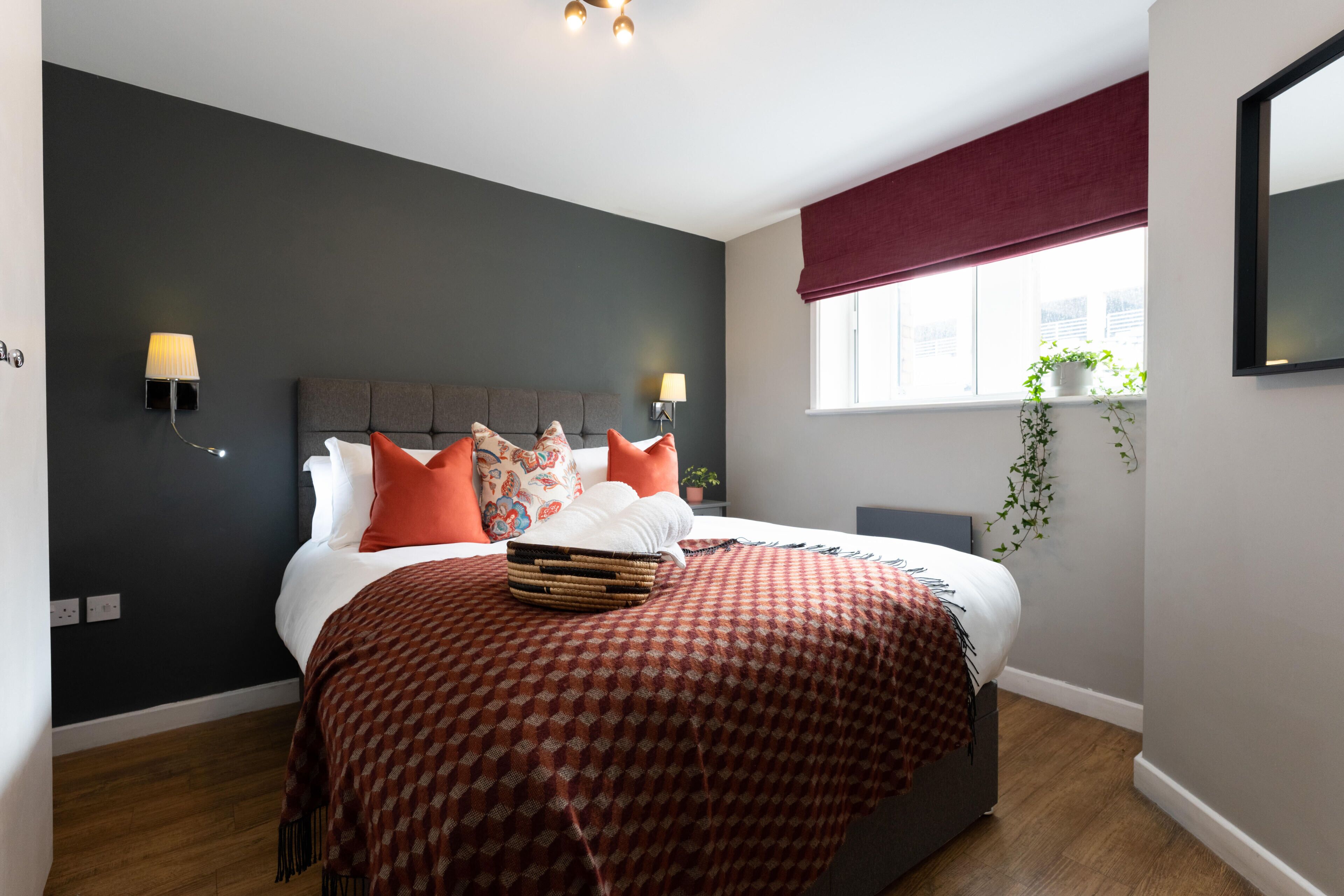 A modern bedroom with a large bed, two bedside lamps, a window with a view, and a plant on the windowsill.