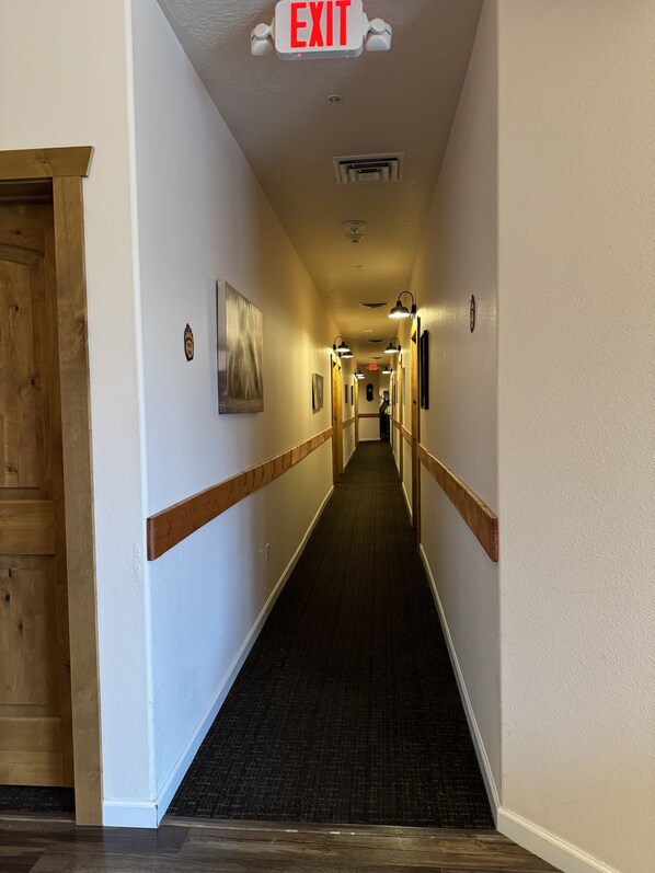 Un pasillo de hotel con letrero de salida, detalles de madera y suelo alfombrado.