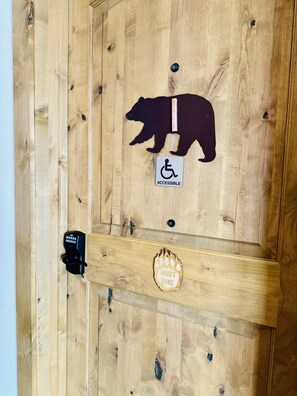 A wooden door with a bear cutout, an accessible sign, a quiet zone sign, and a keypad lock. - Grizzly Lodge Motel (Rathdrum)