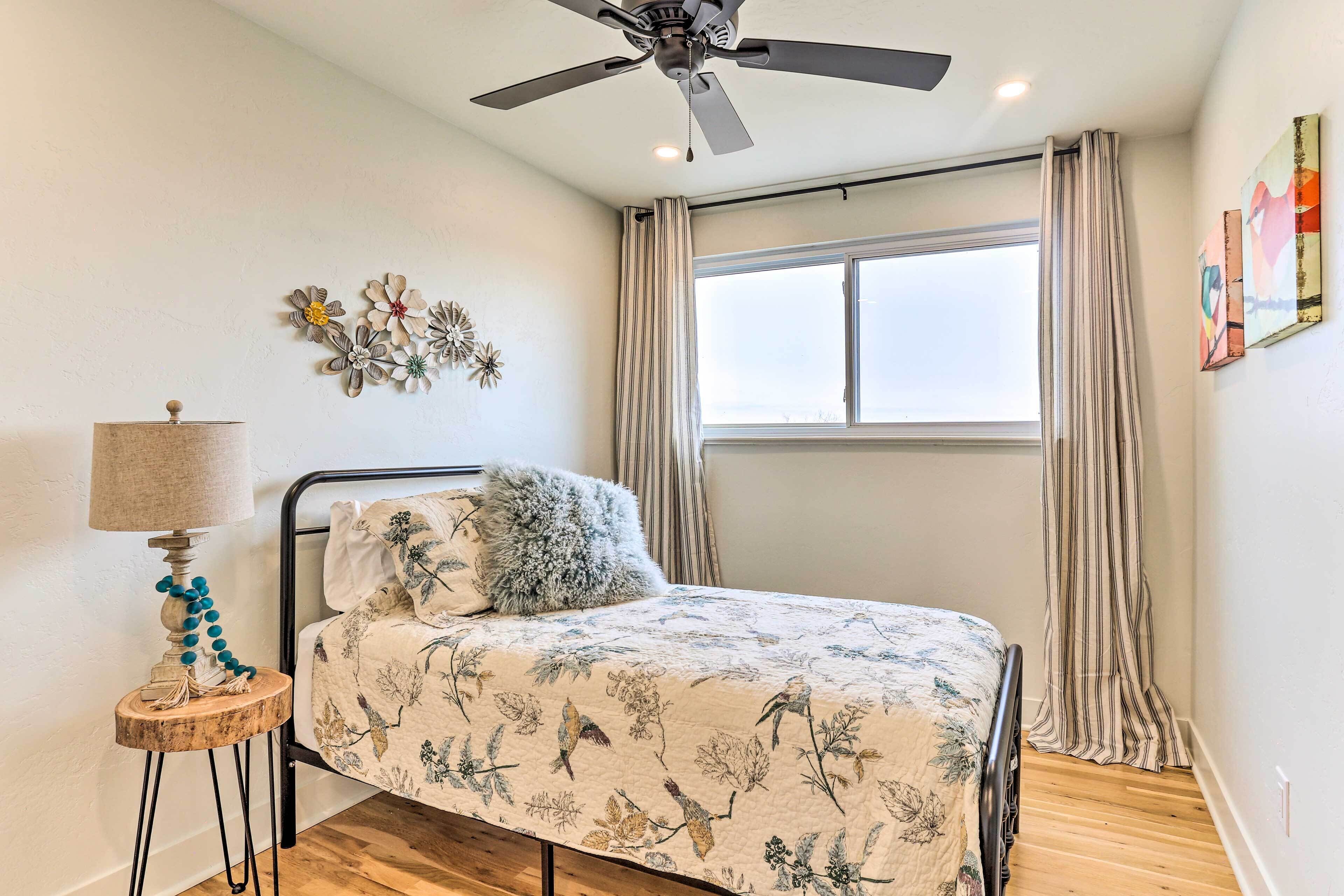 A bedroom with a bed, a ceiling fan, a window with curtains, and wall art.