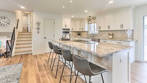 A modern kitchen with white cabinets, a granite island with bar stools, and a staircase leading to another level. - 2 Mi to Dtwn Castle Rock: Home w/ Furnished Patio (Castle Rock)