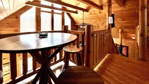 Een houten interieur met een ronde tafel, een plafondventilator en uitzicht door grote ramen.