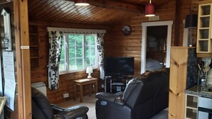 Een gezellig houten interieur met een bank, twee stoelen, een televisie en een kleine tafel.