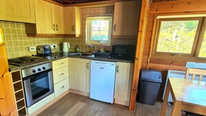 Een kleine keuken met houten kastjes, een inbouwoven, een vaatwasser en een raam dat voor natuurlijk licht zorgt.