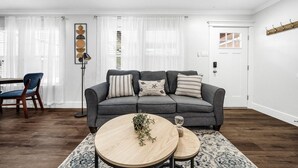 Een moderne woonkamer met een grijze bank, een ronde salontafel en een eethoek met een houten tafel en stoelen.