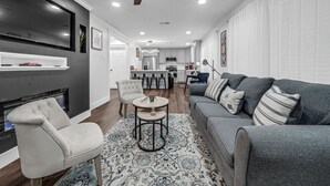 Een moderne woonkamer met een grijze bank, een witte fauteuil en een vloerkleed met een patroon.