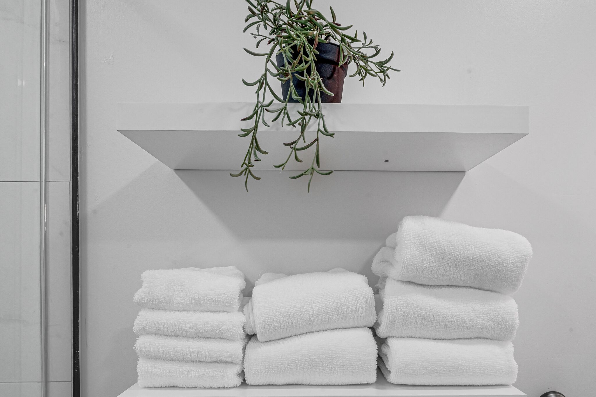 Une salle de bain avec une pile de serviettes blanches et une plante suspendue.