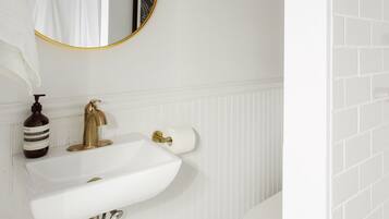 Un baño con lavamanos blanco, detalles dorados, un espejo redondo y un inodoro blanco.