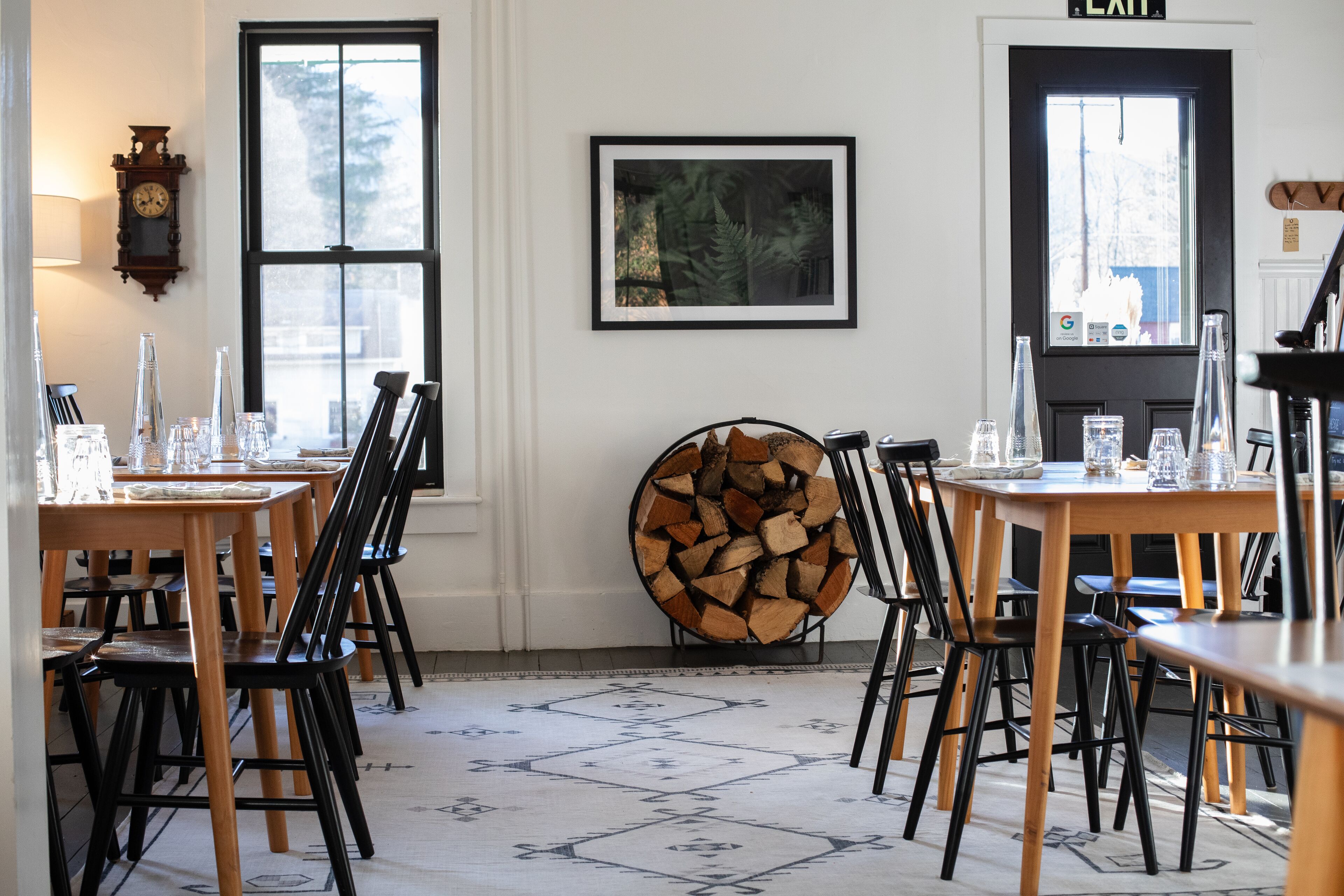 Un comedor con varias mesas y sillas, una chimenea, un reloj y una obra de arte enmarcada en la pared.