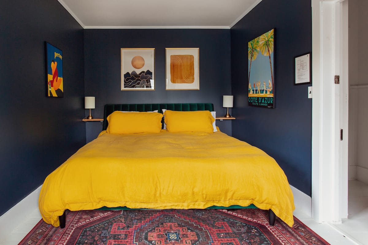 Une chambre à coucher avec un grand lit, des murs de couleur sombre et des œuvres d’art.