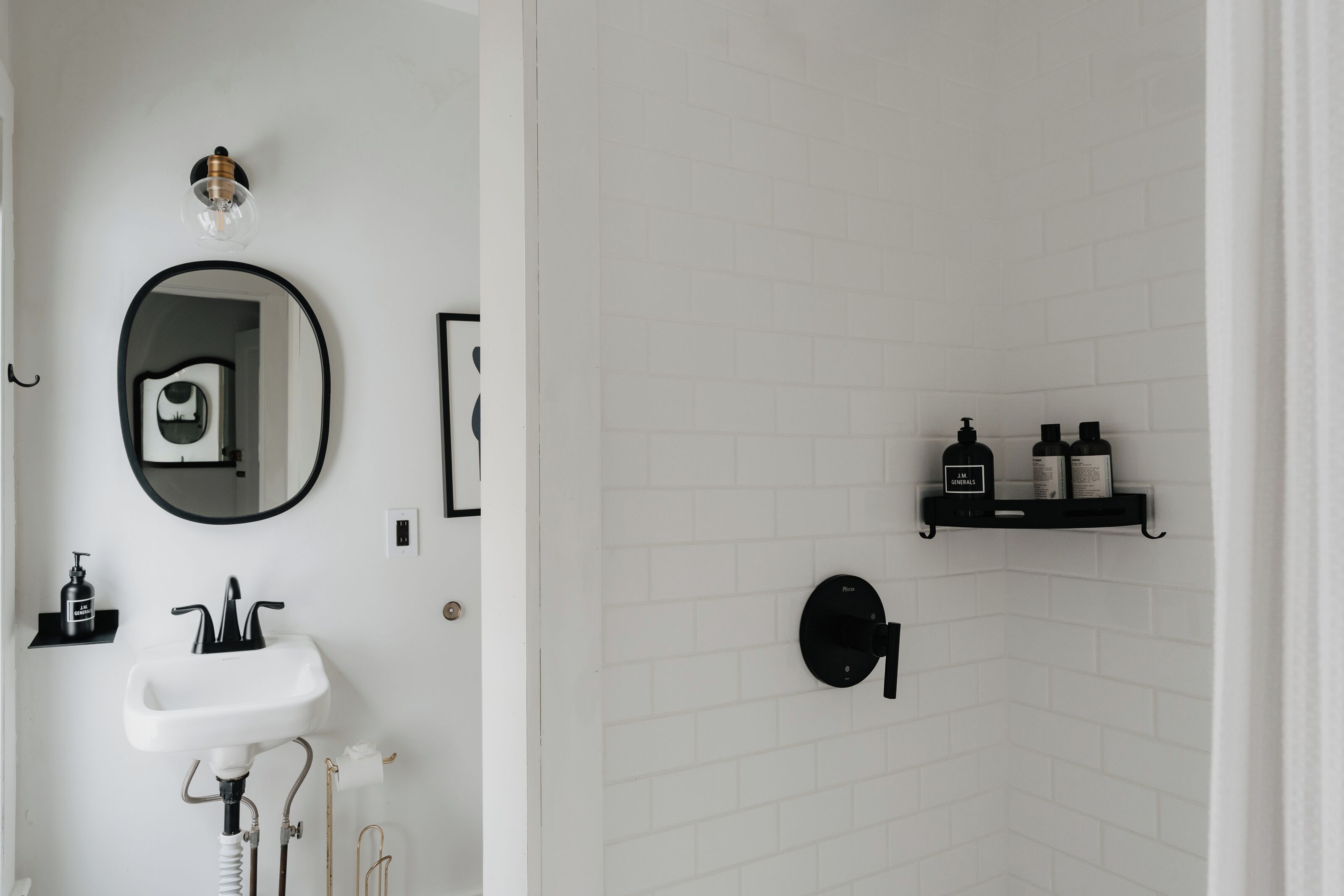 A bathroom with a white sink, a mirror, and a shower area with a black shelf holding toiletries.