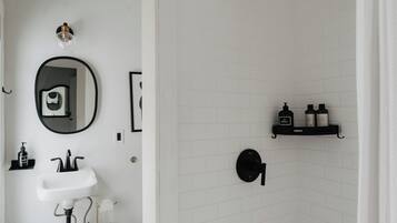 A bathroom with a white sink, a mirror, and a shower area with a black shelf holding toiletries.
