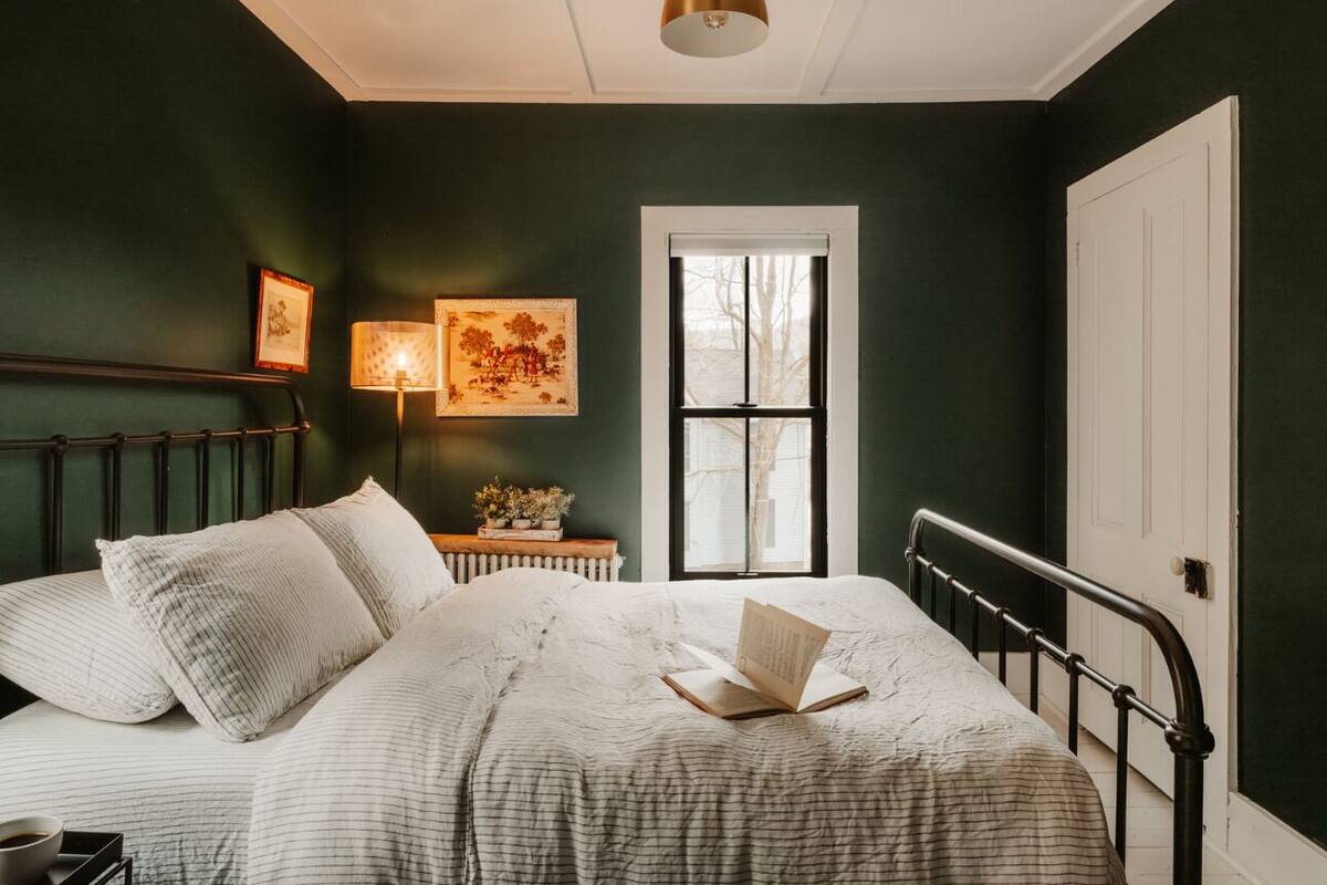 Une chambre à coucher avec un lit, une table de chevet, une lampe, une fenêtre et une porte.