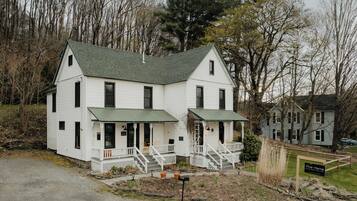 A white two-story house with a green roof, a front porch with steps, and a sign reading "The Yarra."