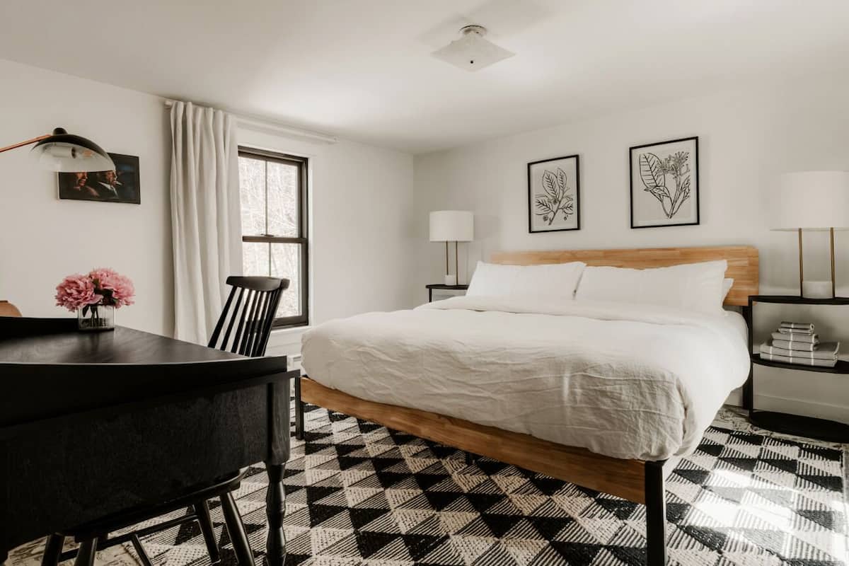 Une chambre d’hôtel avec un lit, un bureau, une chaise, une lampe et des œuvres d’art accrochées aux murs.