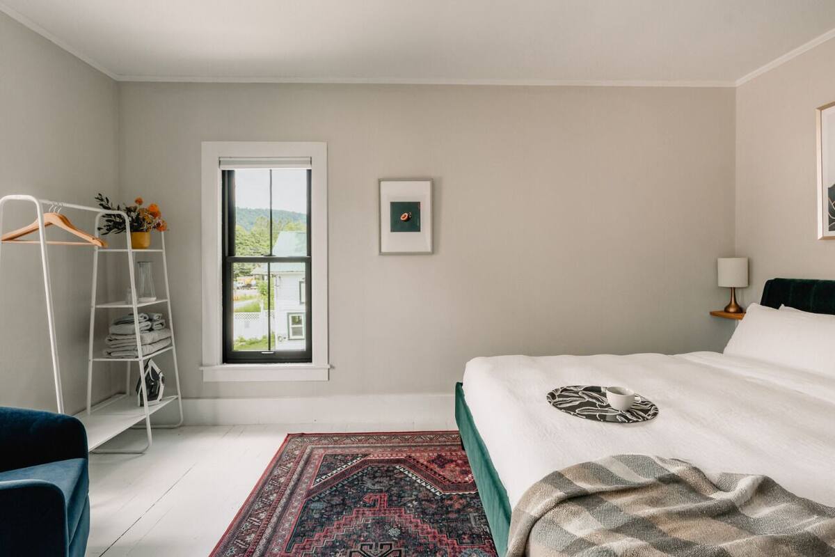 Une chambre à coucher avec un lit, une fenêtre, une étagère avec des vêtements pliés et une vue sur la verdure à l’extérieur.