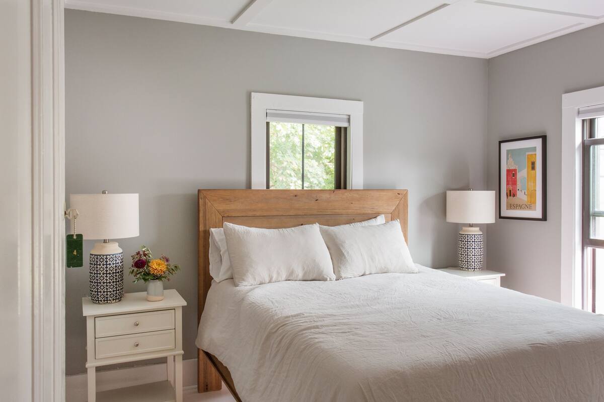 Une chambre à coucher comprenant un lit, deux tables de chevet, une commode, une fenêtre et un tableau encadré accroché au mur.