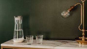 Una mesa de mármol con una jarra de agua, dos vasos y una lámpara de latón frente a una pared oscura.