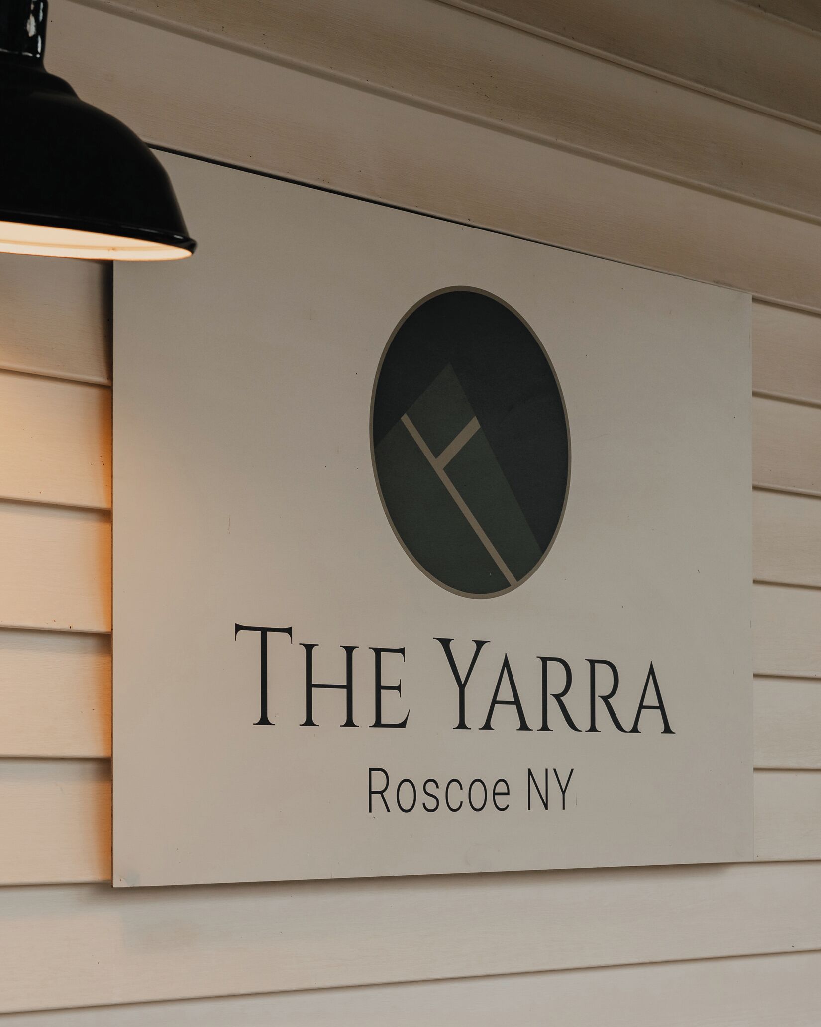 Cartell de 'The Yarra' a Roscoe, NY, amb un disseny minimalista, un logotip circular i el nom de l'establiment.