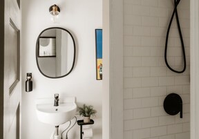 Un baño con lavamanos blanco, un espejo redondo, un cabezal de ducha manual negro y una pequeña planta en maceta.