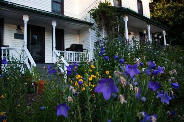 Una casa blanca con un porche y un jardín lleno de flores moradas y amarillas.