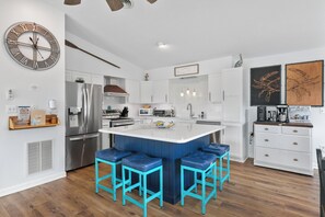 Une cuisine moderne dotée d’un îlot central, de tabourets de bar, d’une grande horloge et de meubles de rangement blancs.
