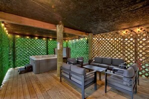 An outdoor patio with wooden flooring, a built-in hot tub, and a seating area with sofas and a table.
