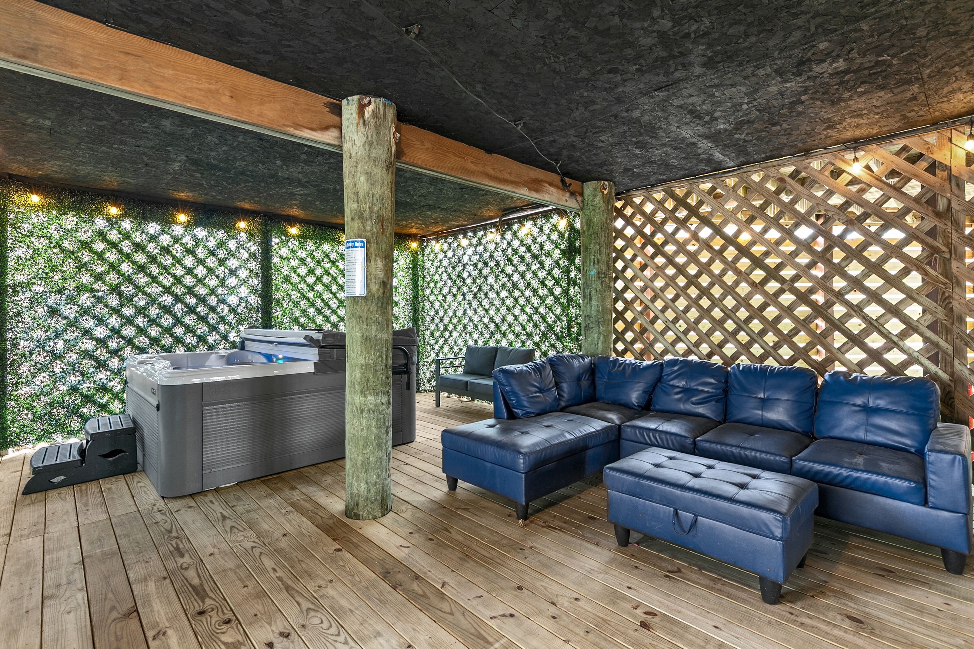 En udendørs terrasse med jacuzzi, en blå lædersofa og et trædeck.