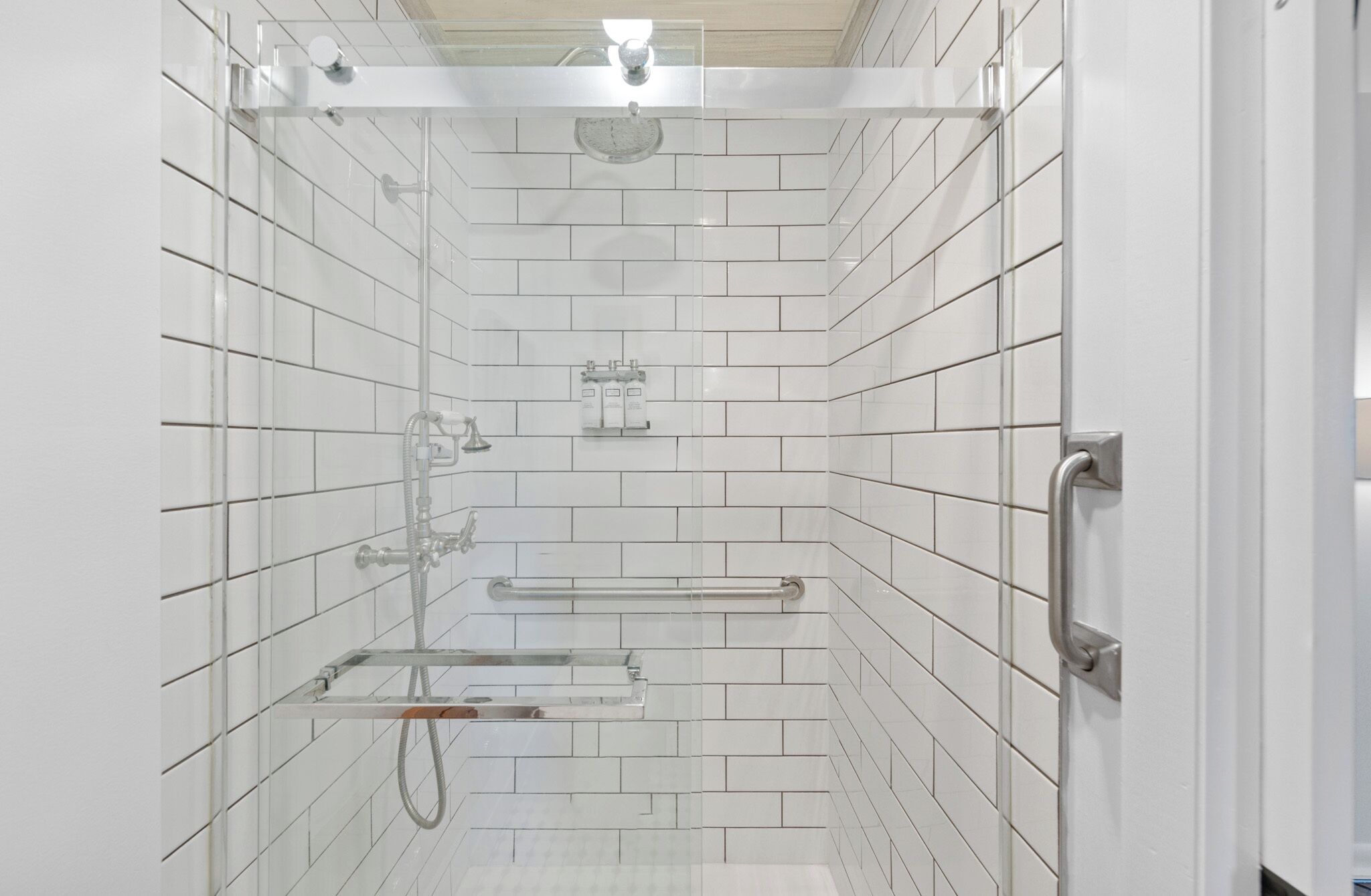 A modern shower with white tiled walls, a glass door, and a metal shower head.