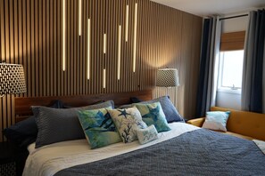 Une chambre d’hôtel avec un mur en lambris de bois, un lit avec plusieurs oreillers, une table de chevet et une fenêtre avec des rideaux.