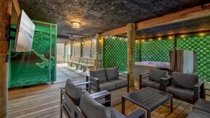A cozy outdoor seating area with wooden flooring, cushioned seating, and a green patterned wall. - Steps to Fenwick Island Beach, Ocean&Bay views, hot tub. Pet & family friendly! (Fenwick Island)