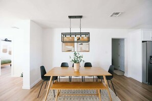 A modern dining area with a wooden table, black chairs, and a hanging light fixture.