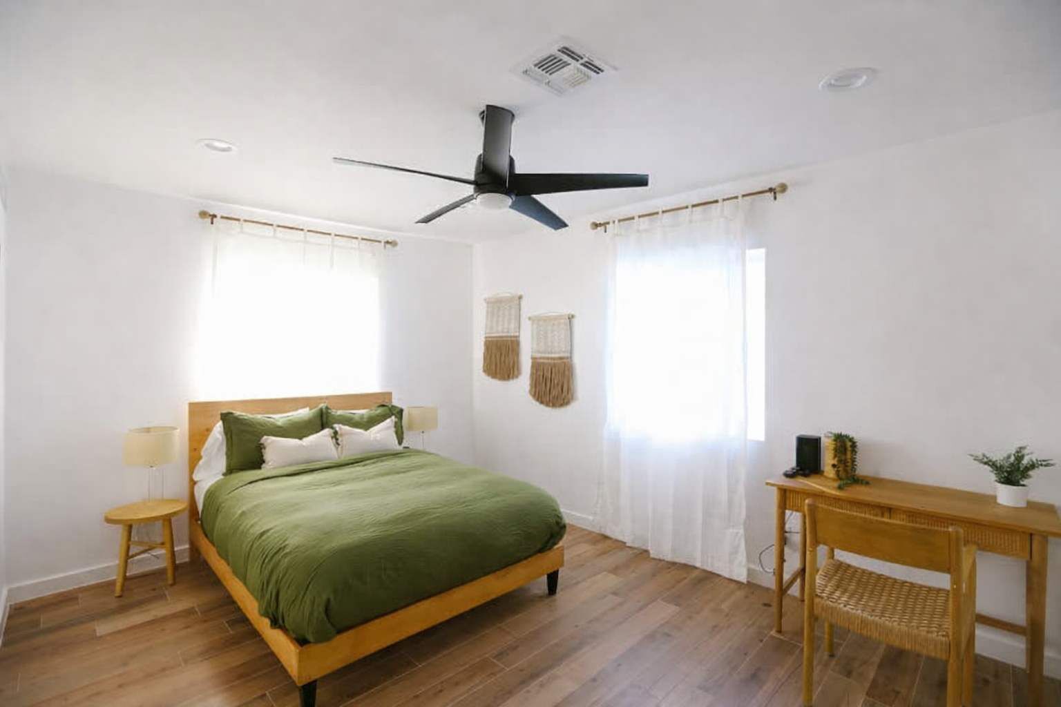 A bedroom with a bed, a ceiling fan, a bedside table, a chair, and a small table with a plant.