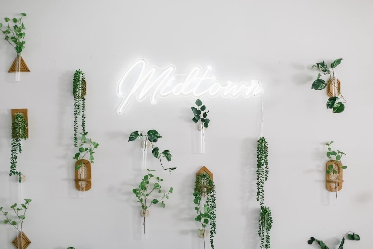 A wall with a neon sign spelling "Midtown" and various hanging plants.