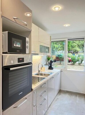Cozinha moderna com eletrodomésticos de aço inoxidável, janela com vista para área verde e design limpo e minimalista.