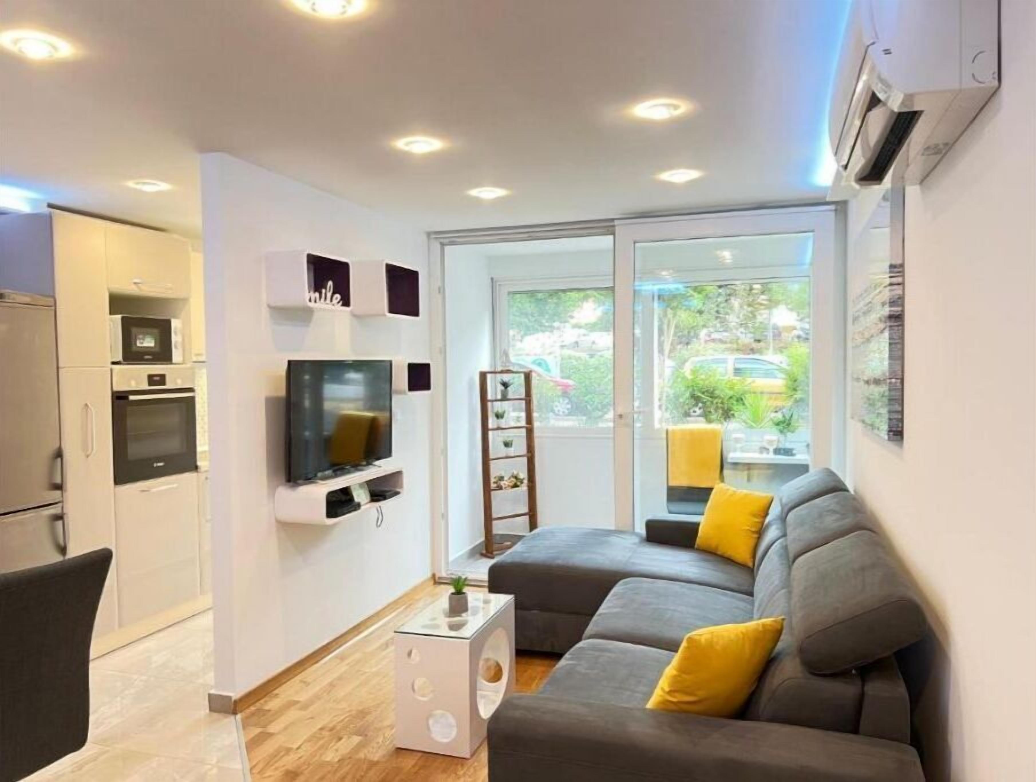 A modern living room with a grey sofa, a flat-screen TV, and a small white side table with a plant.