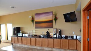 A hotel reception area with a flat-screen TV, a painting of a sunset, a coffee machine, and a vending machine. - Cobblestone Inn and Suites Newton (Newton)