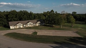 Une grande maison de plain-pied dotée d’une véranda qui fait le tour de la maison, entourée d’une pelouse bien entretenue et d’arbres.