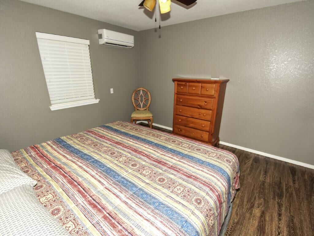 A bedroom with a bed, a dresser, a chair, and a window with blinds.