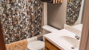 A bathroom with a white toilet, a bathtub with a beige towel, and a sink with a mirror.