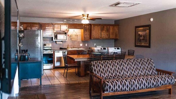 A modern kitchen with wooden cabinets, a dining table, and a patterned sofa. - Lake Texoma Six-Plex Main Room (Mead)