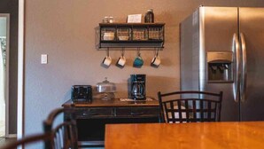 A kitchen with a stainless steel refrigerator, a coffee maker, and a shelf with hanging cups. - Lake Texoma Six-Plex Main Room (Mead)