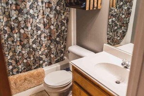 A bathroom with a white toilet, a bathtub with a beige towel, and a sink with a mirror.