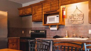 A kitchen with wooden cabinets, a microwave, a stove, and a sink. - Lake Texoma Six-Plex Main Room (Mead)