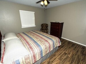 Une chambre à coucher avec un lit, une commode, une chaise et un ventilateur de plafond.