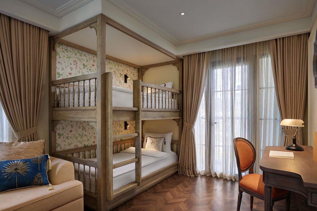 A room with a bunk bed, a sofa, a chair, a desk, and a window with curtains.