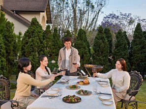 A group of people dining outdoors with a table set for a meal, surrounded by greenery and trees. - Mercure Dalat Resort (Lam Vien - Da Lat)