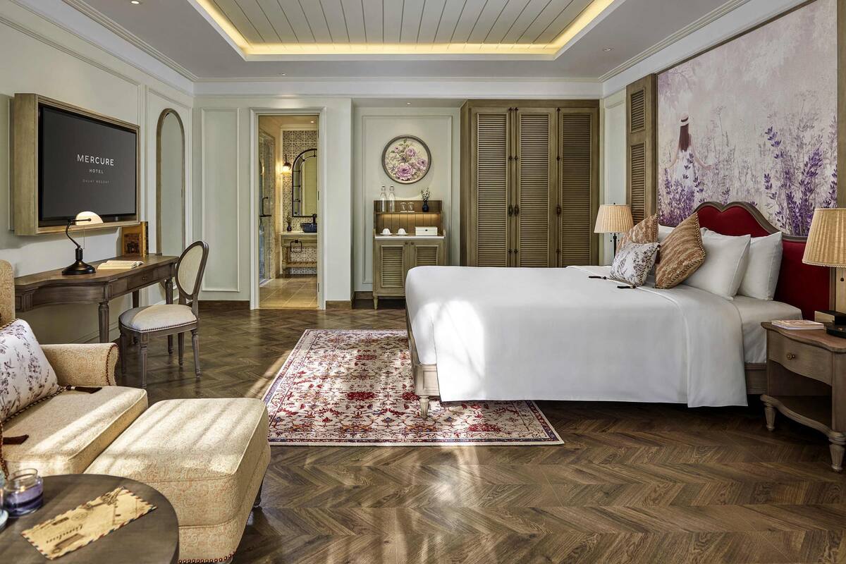 Habitación de hotel con cama, escritorio, silla y televisor en la pared.