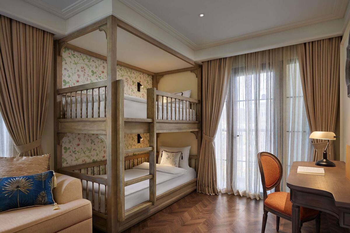 Una habitación con una cama nido, un sofá, una silla, un escritorio y una ventana con cortinas.