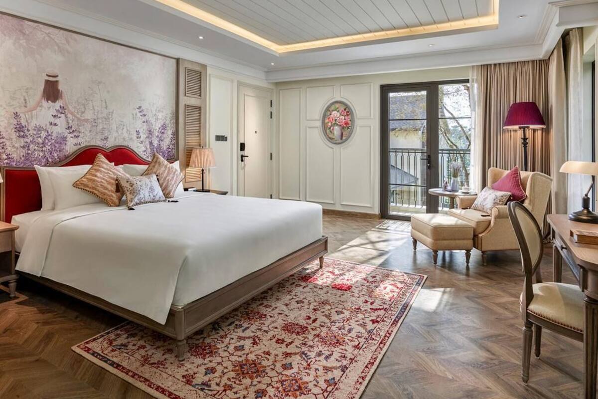 Un dormitorio con una cama grande, una mesita, una silla, un sofá y un balcón con cortinas.